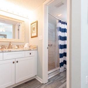 Bright master bath featuring a stylish vanity with a large mirror, plush towels, and a walk-in shower with a striped curtain