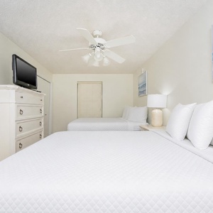 Bright guest bedroom featuring two queen beds, a flat-screen TV, and coastal art, creating a serene and inviting atmosphere