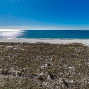 Expansive view of the tranquil gulf and white sand beach from a balcony, framed by lush coastal vegetation and clear skies