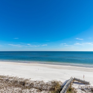 A serene view of the beach front features glowing sand and calm waters under a clear blue sky, inviting relaxation