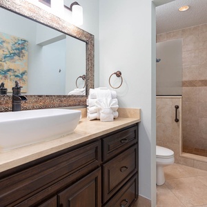 Elegant master bathroom featuring a stylish vessel sink, decorative mirror, and a walk-in shower with textured tile accents