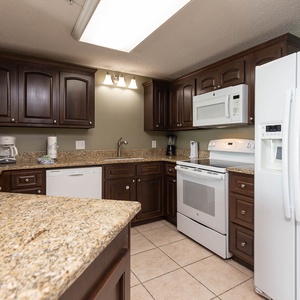 Cook and gather in this spacious kitchen featuring dark wood cabinets, granite countertops, and white appliances