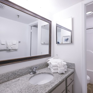 Master bathroom featuring a large mirror, granite countertop, neatly stacked towels, and a tub/shower combo