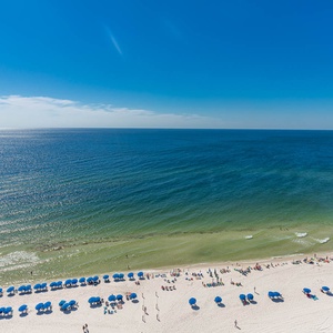 Experience stunning beachfront views with vibrant blue umbrellas lining the sandy shore, perfect for relaxation and fun