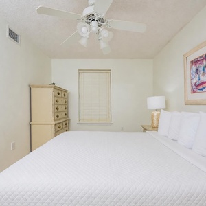 Bright and airy guest bedroom featuring a queen bed, decorative artwork, and a charming dresser with a lamp for a cozy vibe