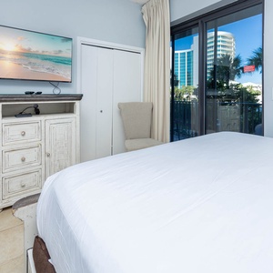 Relax in this comfortable guest bedroom featuring a large TV, a cozy chair, and natural light from the balcony doors