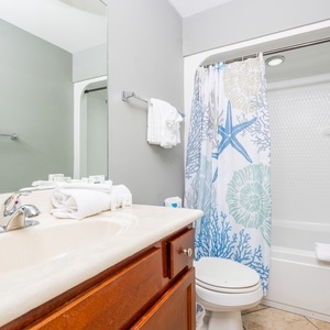 This bathroom features a clean design with a light-colored vanity, fresh towels, and a shower curtain with coastal motifs