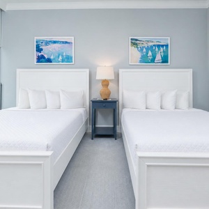 Guests will sleep peacefully in this room featuring two queen beds, decorative artwork, and large windows