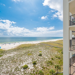Expansive beachfront view showcases white sand and vibrant beach umbrellas under a sunny sky from the balcony