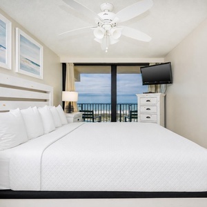 This bedroom features a plush white bed, a TV, and a stunning beachfront view through large sliding glass doors