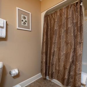 This bathroom features a shower with a stylish brown leaf-patterned curtain, fresh towels, and charming shell artwork