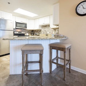 Bright kitchen area features granite countertops, stainless appliances, and a breakfast bar with two stylish stools