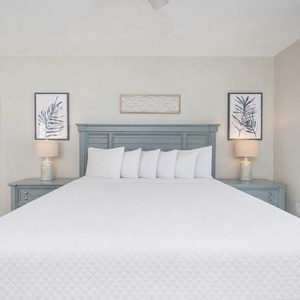 Soft pillow arrangements invite rest in the master suite framed by calming coastal artwork and gentle lamp glow
