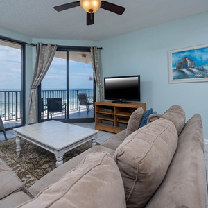 Relax in the inviting living area, featuring a comfortable sofa, a TV, and views through large windows