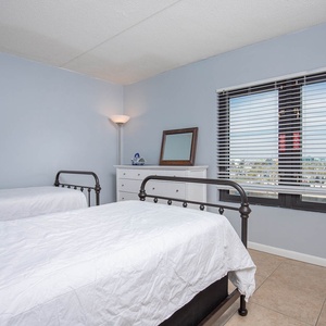 This guest bedroom features two beds, a dresser, and a lovely view through large windows