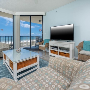 Cozy living area features a large TV, comfortable seating, and a balcony with a beautiful view of the beach