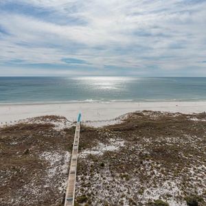 Stunning view of the beach and gulf from a wooden boardwalk leading to the shore, framed by gentle dunes and greenery