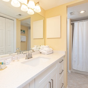 The master bathroom features a bright yellow hue, a vanity with modern fixtures, and neatly stacked towels for a refreshing stay