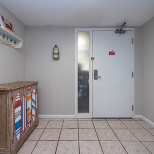 This welcoming entryway features beach-themed decor, a colorful surfboard cabinet, and easy access to the rest of the condo