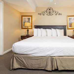 The bedroom features a king bed with decorative pillows, bedside lamps, and a bathroom entry with a floral shower curtain