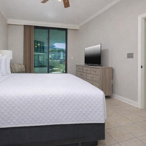 Inviting master bedroom featuring a plush king bed, flat-screen TV, and a view of the balcony through sliding glass doors