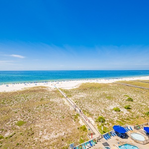 Stunning view of the beach with white sand, turquoise gulf waters, and a pathway leading to the shore from the property