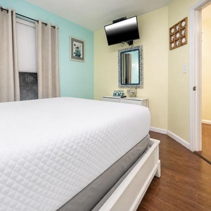 This cozy bedroom features a comfortable bed, a mounted TV, and soft blue-green walls, creating a relaxing atmosphere