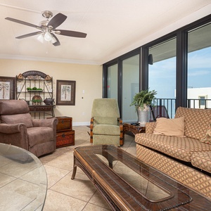 The living area features comfortable chairs and a stylish coffee table, with a stunning beach view through large windows