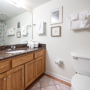 Bright guest bathroom featuring a dark granite countertop, decorative beach-themed art, and neatly arranged white towels