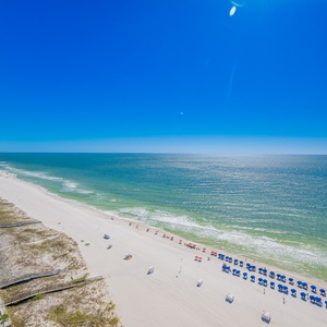 Beach view lined with colorful umbrellas under a clear blue sky from a spacious balcony