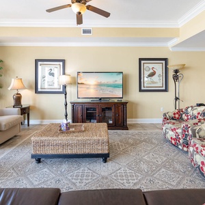 Bright and inviting living area featuring colorful floral chairs, a cozy coffee table, and a large flat-screen TV