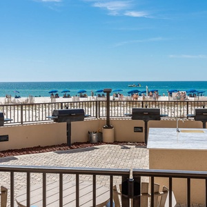 Enjoy grilling in the outdoor pool area, overlooking the beach and vibrant umbrellas on the shore