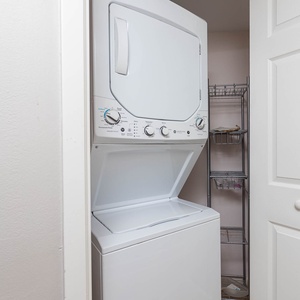 Stacked washer and dryer in a compact laundry nook, complemented by a metal shelving unit for added storage convenience