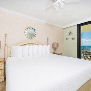 Bright master bedroom featuring a king bed, decorative mirror, and a TV, with the balcony offering a view of the beach front