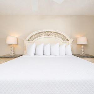 A beautifully styled master suite features a large bed with crisp white linens, with elegant lamps on ornate nightstands