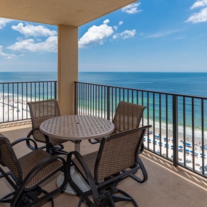 Enjoy a relaxing moment on the balcony with a table and chairs, overlooking the beach and vibrant umbrellas along the shore