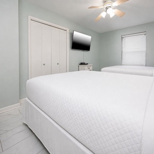 Bright guest bedroom featuring two queen beds, a wall-mounted TV, and light green walls, creating a refreshing retreat