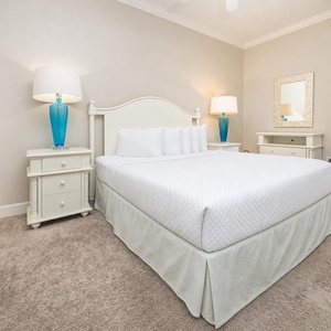 This guest bedroom features a king bed, bright blue lamp, soft carpet, and a large mirror, creating a serene atmosphere