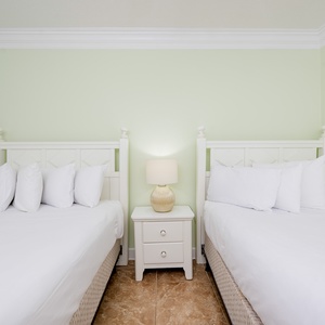 Rest in this serene guest room featuring two double beds, soft linens, and a calming green hue for a peaceful retreat