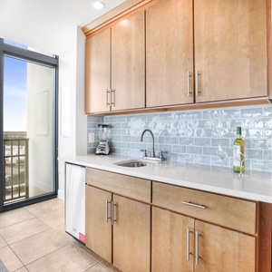 This sleek wet bar features warm wood cabinetry, a stylish backsplash, blender, and a stunning view through large windows