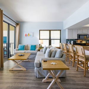 Airy living area featuring cozy seating, stylish decor, and a view of the balcony through large sliding doors