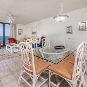 Dining area features a glass-top table with wicker chairs, complemented by red leather armchairs and a scenic gulf view