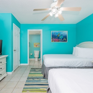 Bright cheerful walls complement two double beds in this guest room, featuring a TV and a vibrant area rug for a fun vibe