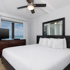 King master suite featuring a plush bed, a large TV, and stunning views of the beachfront through expansive windows