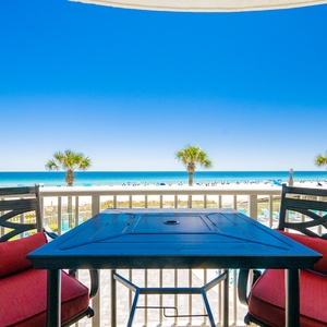 Relax on the cozy balcony with red seating, overlooking the beach and inviting pool area under a bright blue sky