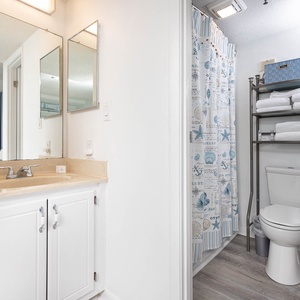 The bathroom features a clean design with a spacious vanity, bright mirrors, and a charming beach-themed shower curtain