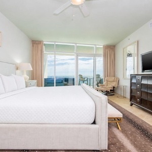The master bedroom features a plush king bed, a TV, and a stunning beachfront view with direct balcony access
