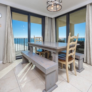 The dining area features a rustic wood table with bench seating, framed by a beautiful beach front view