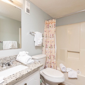 The bathroom features a clean design with a spacious vanity, fresh towels, and a shower curtain adorned with a floral pattern