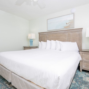 Spacious bedroom features a king bed with crisp white linens, a decorative blue lamp, and soft area rug for added comfort